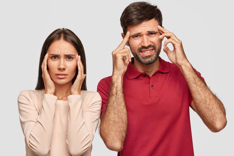 Mulher e homem com as mãos na cabeça sentindo dor.