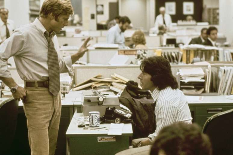 O ator americano Robert Redford vestindo uma camisa branca com calças marrons e uma gravata estampada, em conversa com o ator americano Dustin Hoffman, que está sentado em uma camisa listrada, em uma recriação dos escritórios do The Washington Post em 'Todos os Homens do Presidente', filmado no Burbank Studios em Burbank, Califórnia, 1976. O thriller político baseado no escândalo de Watergate, dirigido por Alan J Pakula, estrelou Redford como Bob Woodward e Hoffman como Carl Bernstein. (Foto de Michael Ochs Archives/Getty Images)