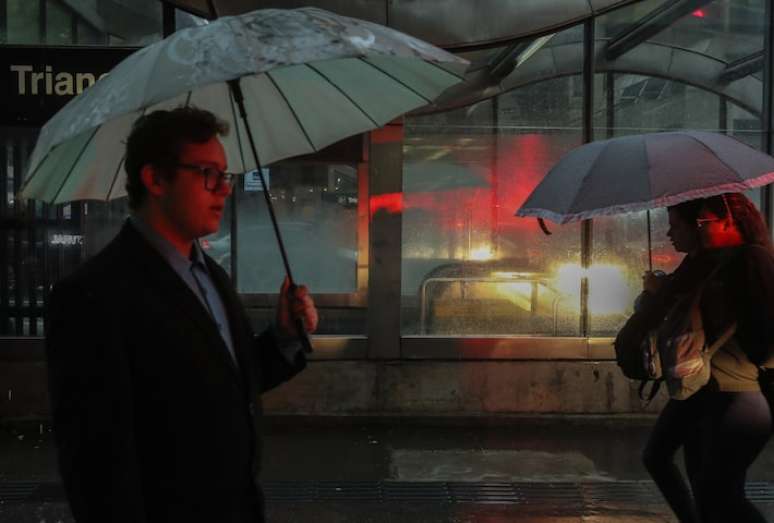 Na foto, pedestres se protegendo de chuva na cidade de São Paulo.