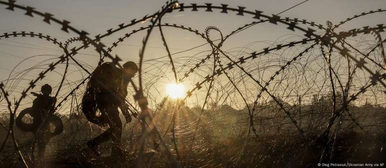 Dois soldados passam por uma cerca de arame farpado na linha de frente de Donetsk