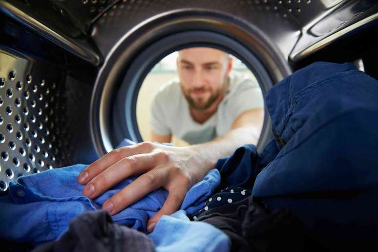 Vista de dentro da máquina de lavar com um homem estendendo a mão e puxando a roupa limpa.