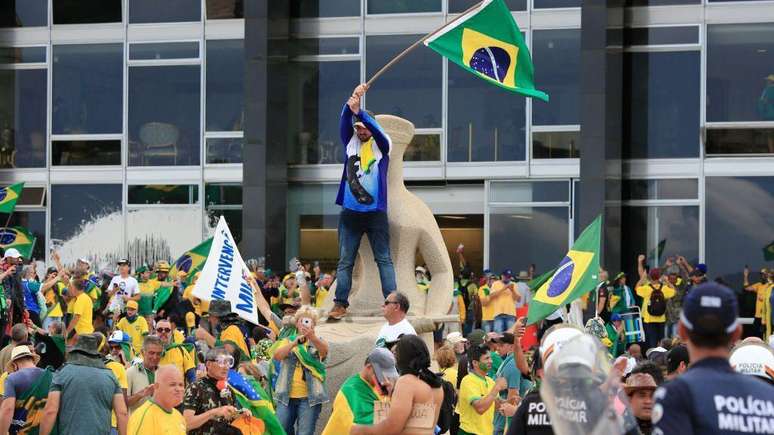 Pessoas em volta e em cima de estátua que representa a Justiça em frente ao STF