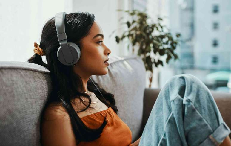 Pessoa usando fones de ouvido, ouvindo música enquanto está sentada no sofá