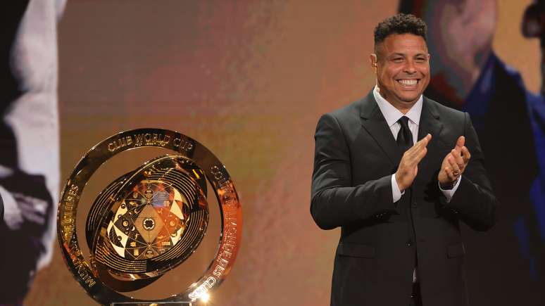 O ex-jogador de futebol brasileiro Ronaldo Nazário reage ao lado do troféu da Copa do Mundo de Clubes da FIFA durante o sorteio da Copa do Mundo de Clubes nos Estúdios Telemundo.