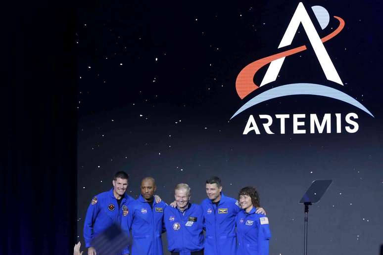 Cinco pessoas em macacões azuis em frente a uma tela que mostra o logotipo da Artemis.