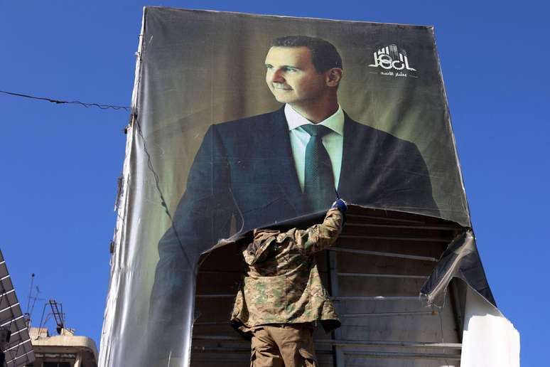 Combatente rebelde rasga um retrato de Bashar al-Assad em Aleppo, na Síria