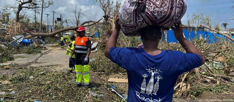 Homem carrega seus pertences enquanto equipes de resgate tentam desbloquear uma estrada em Mayotte