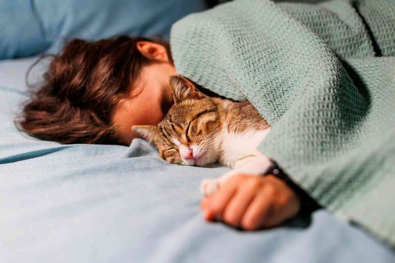 Uma pessoa dorme na cama com seu gato.