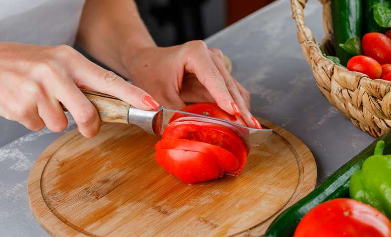 Mulher cortando tomate em uma tábua de corte.