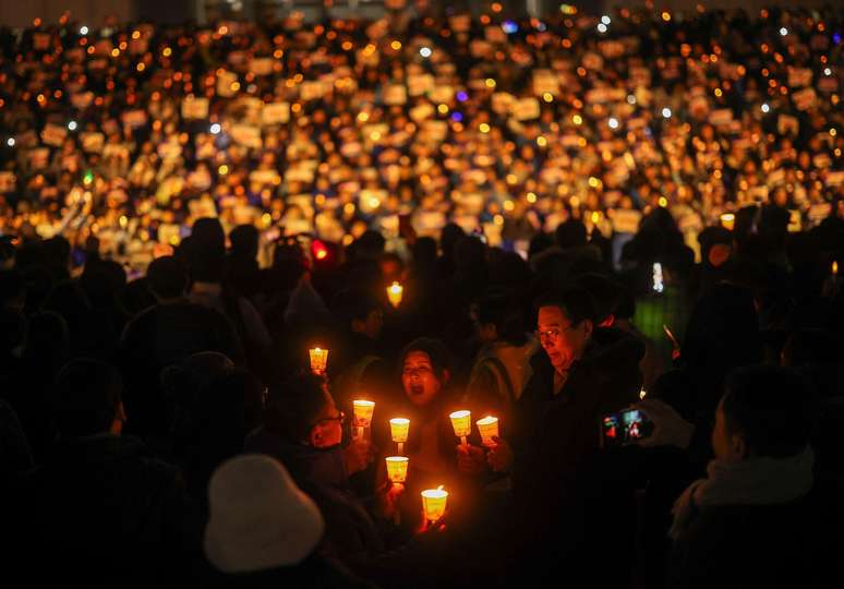 Pessoas seguram velas e cartazes durante uma vigília para exigir a renúncia do presidente sul-coreano, Yoon Suk Yeol, na Assembleia Nacional em Seul, em 5 de dezembro de 2024, após ele ter decretado lei marcial (que foi revogada horas depois)