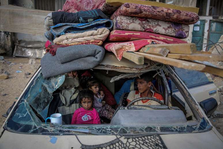 Palestinos desalojados entram dentro de um carro destruído, enquanto fogem de áreas na zona leste de Khan Younis, no sul da Faixa de Gaza, em 7 de outubro de 2024