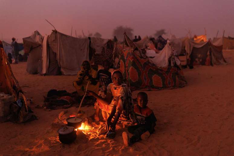 Refugiados sudaneses recém-chegados cozinham em fogueiras do lado de fora de seus abrigos improvisados ​​ao anoitecer, perto de um acampamento de realocação em 24 de abril de 2024, perto de Adre, no Chade