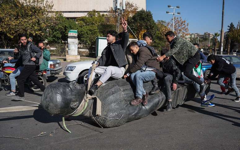 Estudantes arrastam uma estátua derrubada do falecido presidente Hafez al-Assad pela rua durante uma manifestação perto do campus da Universidade de Damasco, na capital síria, em 15 de dezembro