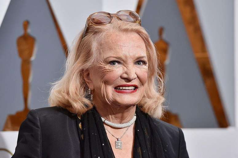 Gena Rowlands sorri para a a foto. Usa roupas sociais, brinco e colar.