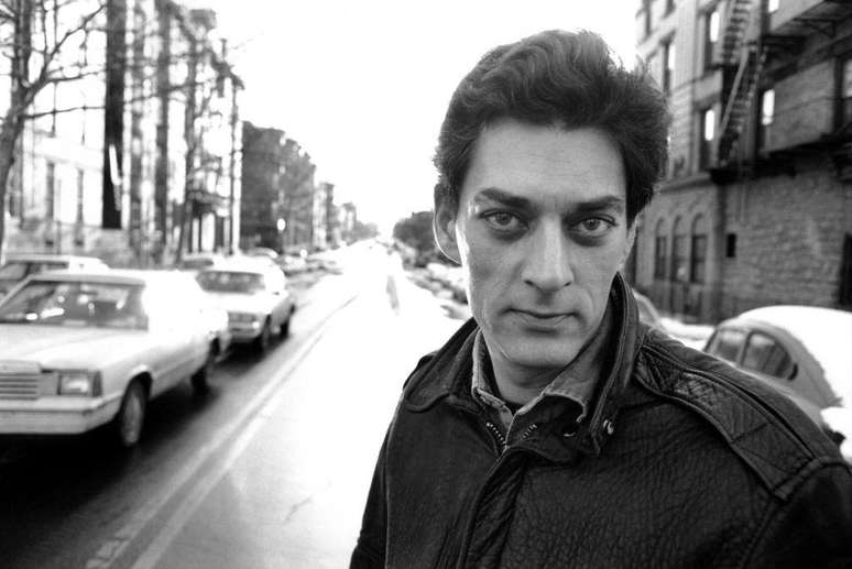 Paul Auster com rua ao fundo e carros estacionados