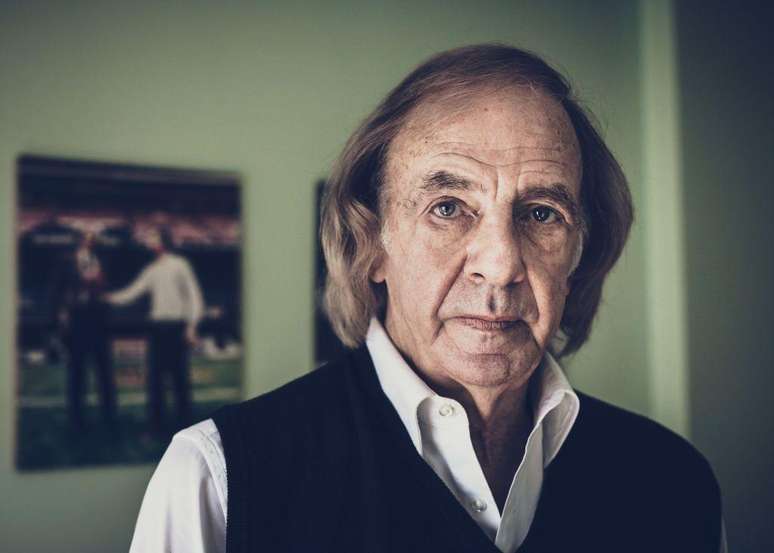 Luis Menotti de roupa social, com quadro ao fundo desfocado