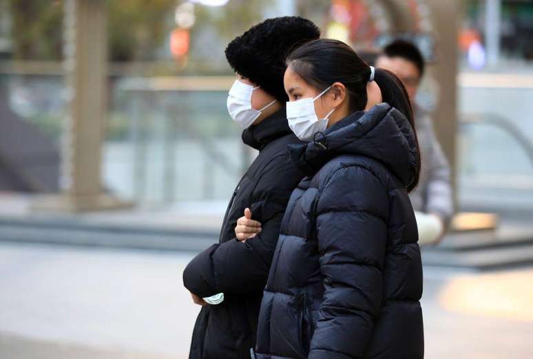 Duas pessoas caminham na rua usando máscaras de proteção da boca e nariz