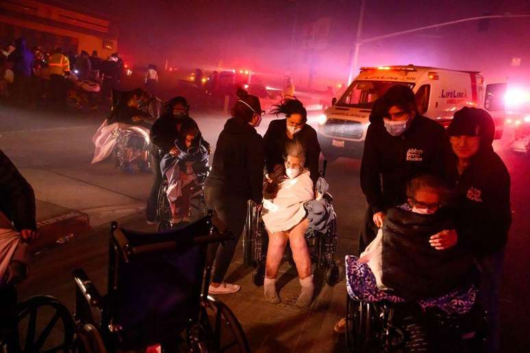 Pacientes idosos são levados para veículos de emergência enquanto brasas e chamas se aproximam durante o incêndio em Pasadena, na Califórnia