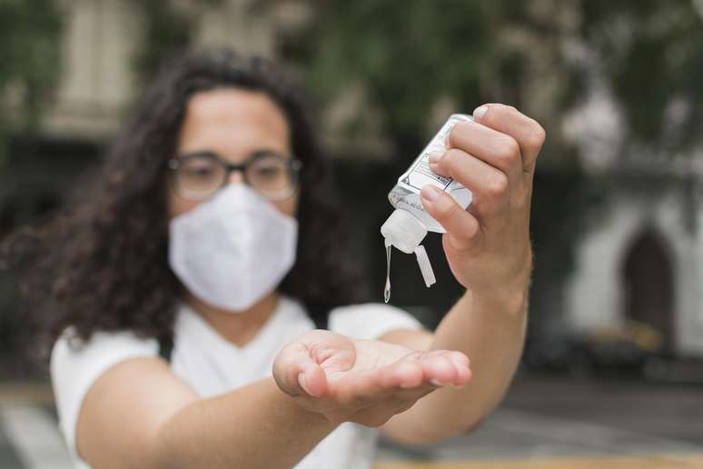 Mulher com máscara de proteção usando álcool em gel nas mãos.