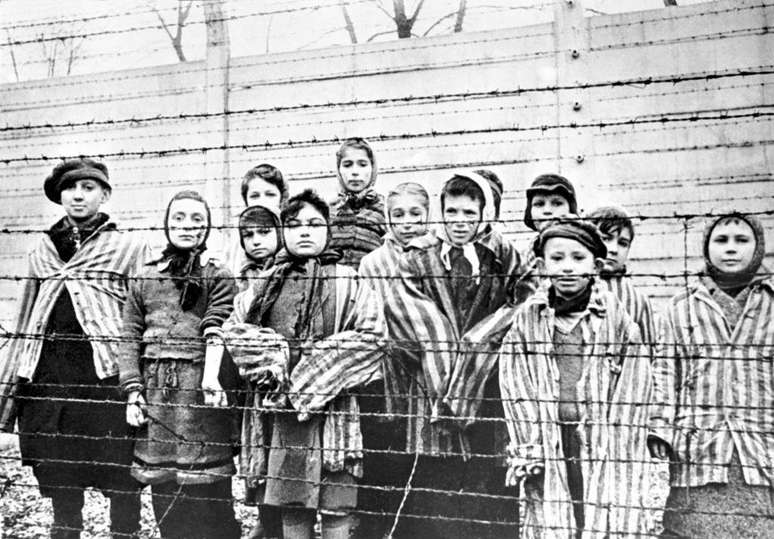 Um grupo de crianças sobreviventes atrás de uma cerca de arame farpado no campo de concentração nazista de Auschwitz