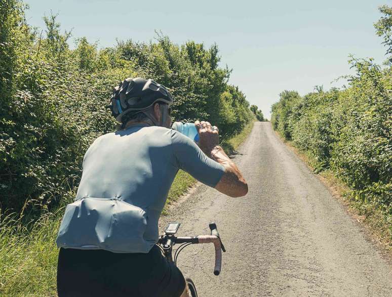 Um homem andando de bicicleta enquanto bebe uma bebida esportiva azul.