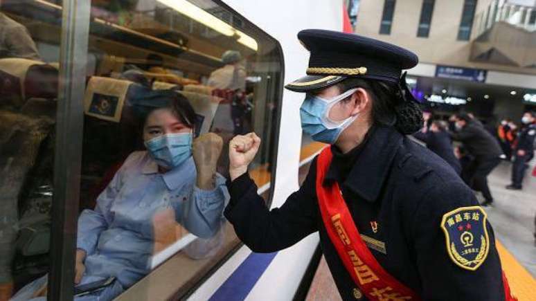 Os primeiros casos de uma 'pneumonia misteriosa' começaram a chamar a atenção na China no final de dezembro de 2019. Nesta foto, de fevereiro de 2020, uma funcionária do sistema ferroviário chinês (à direita) saúda uma profissional de saúde que se dirigia a Wuhan, o primeiro epicentro da crise sanitária.