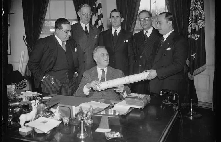Da esq. para a dir.: Francisco Lopes da Cruz; o intérprete S. W. White; Leônidas Borges de Oliveira; Mário Fava; e Fernando Lobo segurando o conjunto de 32 mapas feitos durante a viagem. Sentado: Franklin Delano Roosevelt 