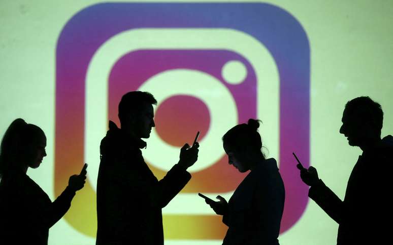 Pessoas utilizando o celular diante da logo do Instagram