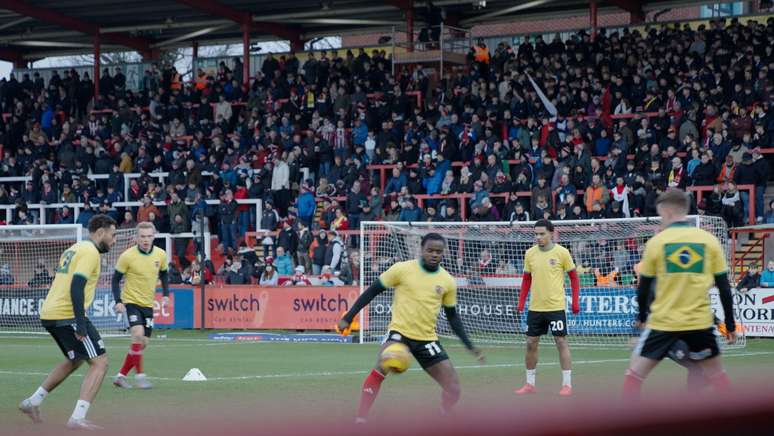 Jogadores do Exeter City aquecem no gramado com uma camisa verde e amarela antes do jogo contra o Bolton Wanderers
