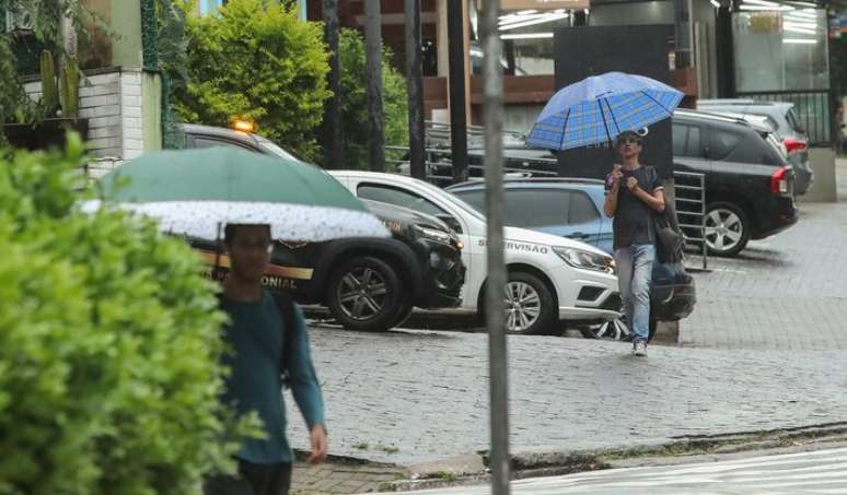 Na foto, pedestres se protegem de chuva, na zona sul de São Paulo.