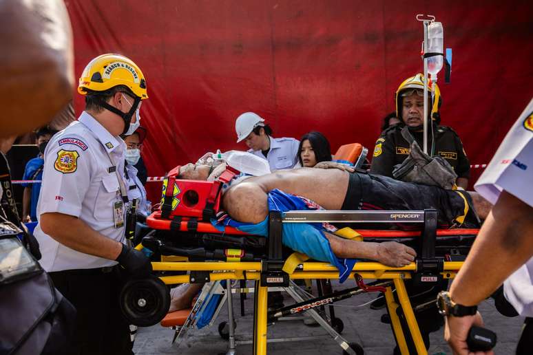 Um trabalhador da construção civil ferido é transportado para fora de um prédio desabado na Tailândia.