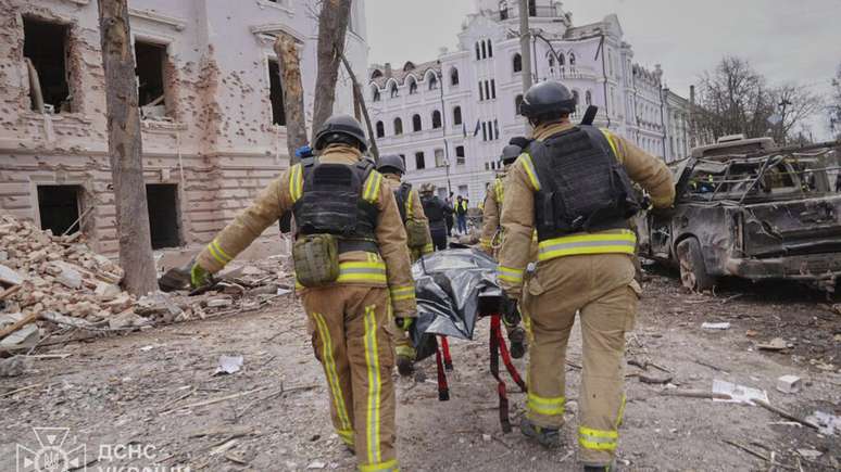 Bombeiros carregam corpo de uma vítima do bombardeio russo contra a cidade de Sumy, no nordeste da Ucrânia, neste domingo, 13 de abril de 2025.
