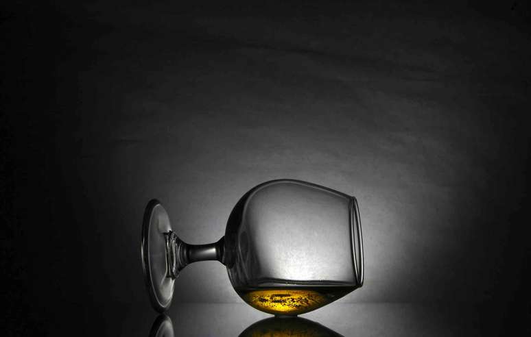 Copo de Snifter com líquido âmbar de lado contra fundo escuro