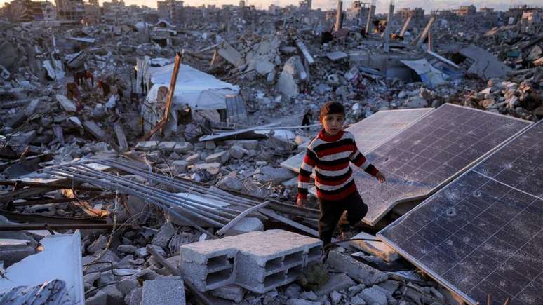 Menino caminha em meio a painéis solares destruídos nos escombros de construções bombardeadas por Israel em Jabaliya, no norte da Faixa de Gaza. 14 de abril de 2025
