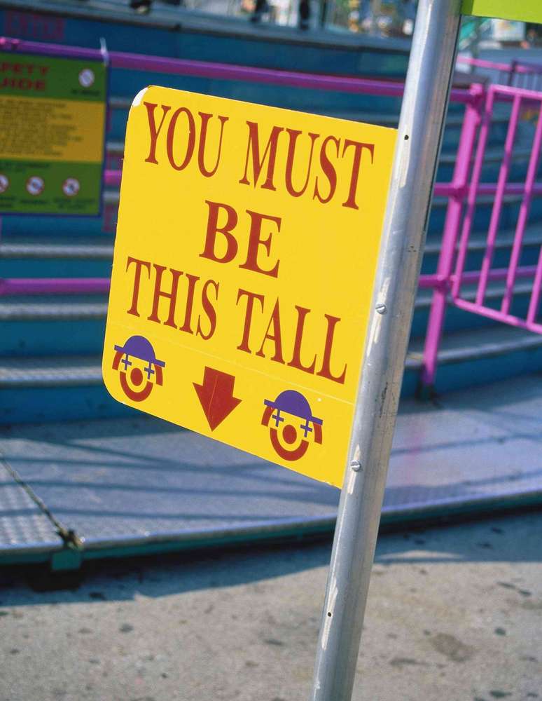 Placa com dois rostos de palha&ccedil;o onde se l&ecirc; 'VOC&Ecirc; DEVE SER T&Atilde;O ALTO' com uma seta