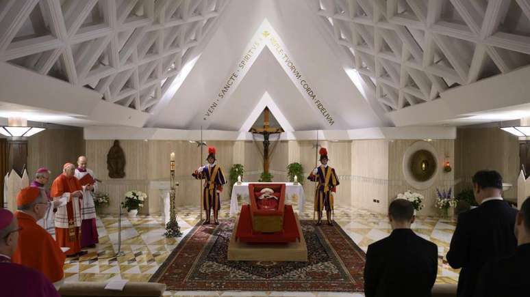 O papa Francisco em seu caixão aberto, vestido com uma túnica vermelha, com a mitra papal na cabeça e um rosário na mão