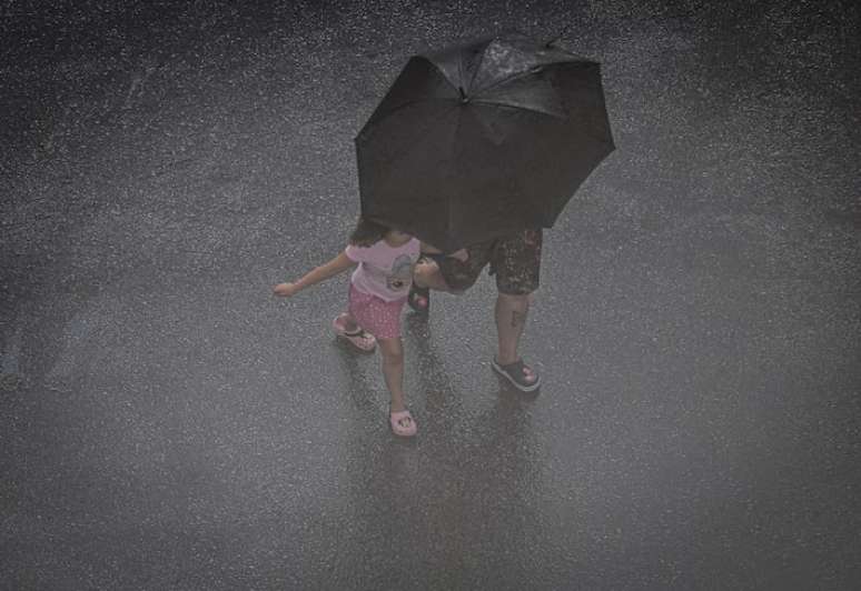 Na imagem, pedestres se protegem de chuva.