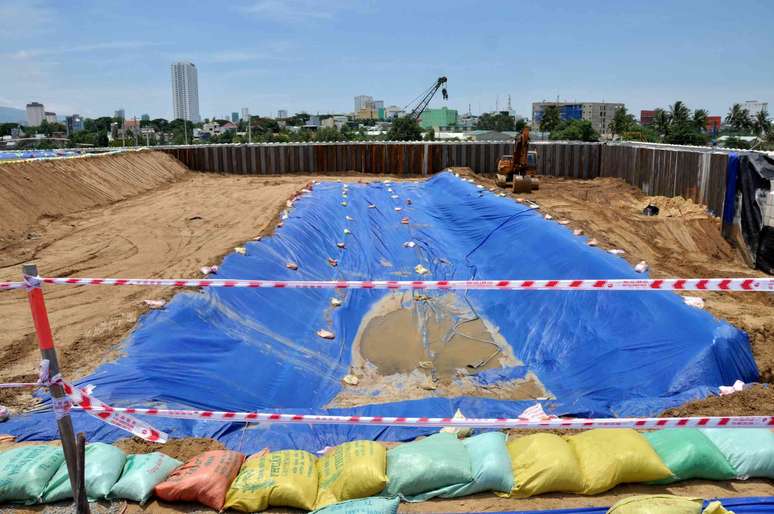 Um poço com sacos de areia e lonas e edifícios ao fundo.