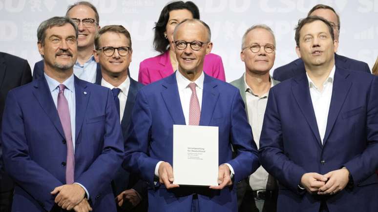 O l&iacute;der da CSU, Markus Soeder, o l&iacute;der da CDU, Friedrich Merz, e o l&iacute;der do SPD, Lars Klingbeil, na primeira fila da esquerda, est&atilde;o juntos com os novos ministros ap&oacute;s a assinatura do tratado de coaliz&atilde;o em Berlim, nesta segunda-feira (5)