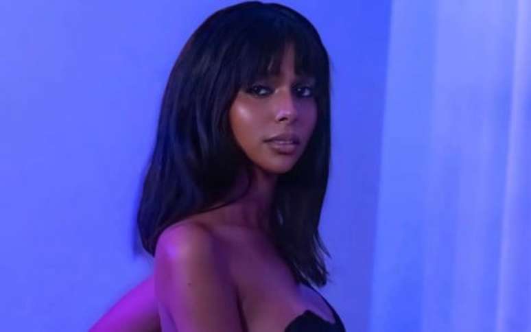 Ella Viana posando em frente a um fundo totalmente azul, usando lingerie preta