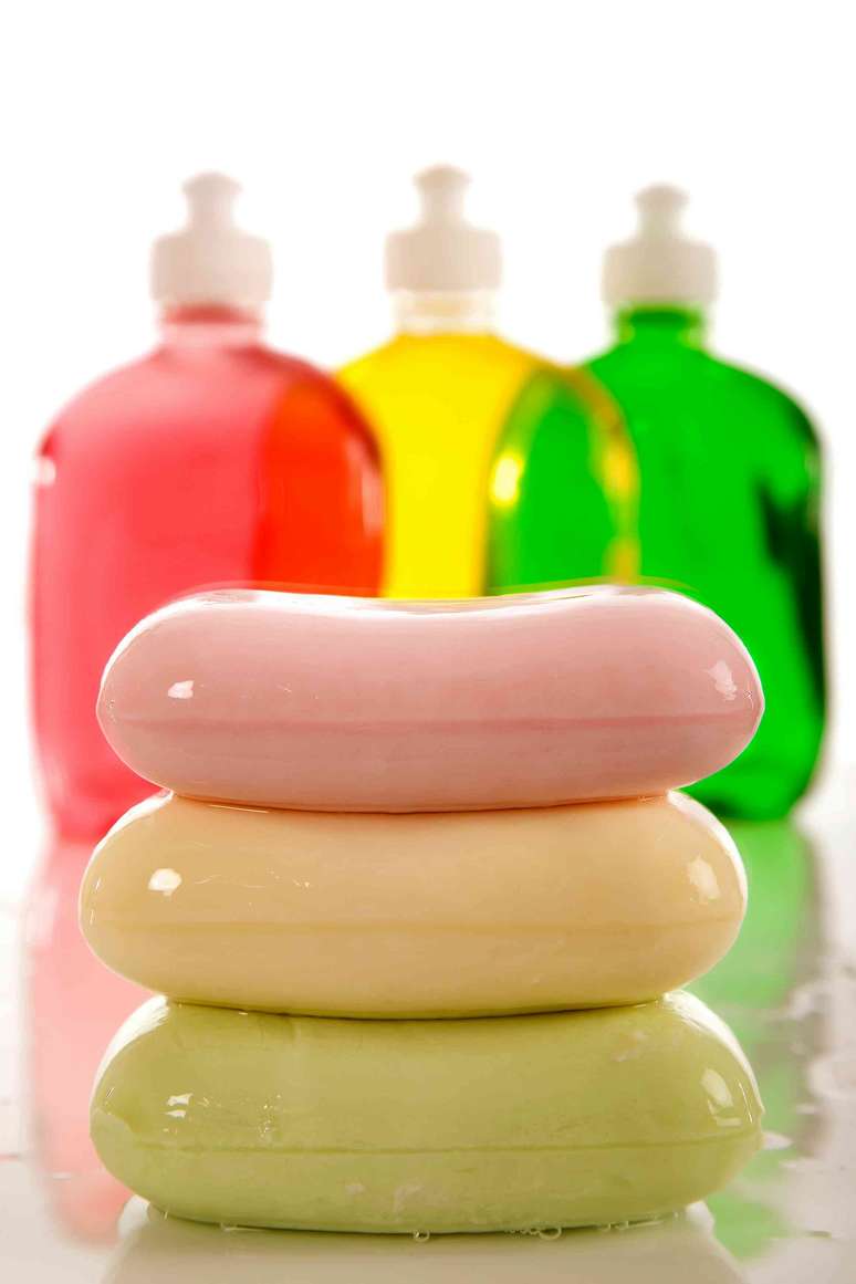 tr&ecirc;s barras de sab&atilde;o coloridas em frente a tr&ecirc;s frascos coloridos de sabonetes transparentes
