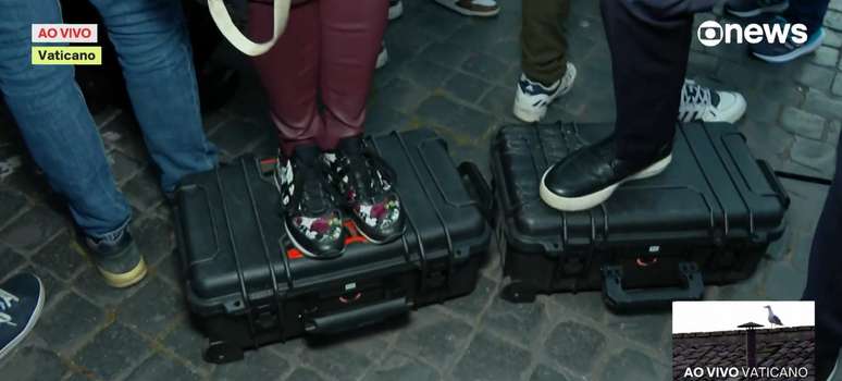 Bianca Rothier e Nilson Klava usam as maletas das câmeras e microfones para ganhar altura no meio da multidão no Vaticano