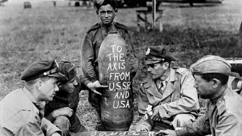 Aviadores dos EUA e da URSS preparam uma mensagem conjunta com os dizeres 'para o eixo da URSS e dos EUA' para o inimigo nazista em uma base aérea na Rússia usada por aeronaves americanas