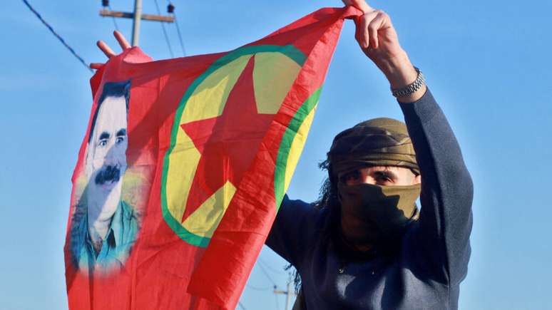 Na imagem, uma mulher curda agita uma bandeira com o retrato do fundador do Partido dos Trabalhadores do Curdistão (PKK), Abdullah Öcalan, enquanto as pessoas se reúnem para ouvir uma mensagem de áudio do líder preso.