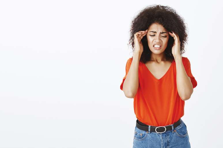 Poor girl having terrible headache. Studio shot of upset european female with afro haircut, touching temples and frowning, grimacing from pain, suffering migraine and standing unfocused. Copy space