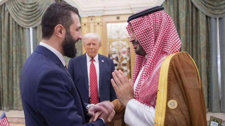 Presidente dos Estados Unidos, Donald Trump (ao fundo), entre o presidente interino da Síria, Ahmed al-Sharaa (esq.), e o príncipe herdeiro saudita, Mohammed bin Salman em Riade em 14 de maio de 2025.