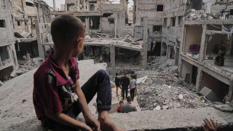 Criança palestina observa escombros de casas destruídas por ataques aéreos israelenses em Khan Yunis, na Faixa de Gaza, na quinta-feira, 15 de maio de 2025.