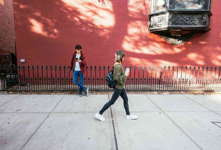 Uma jovem passa por um jovem que est&aacute; olhando para seu telefone