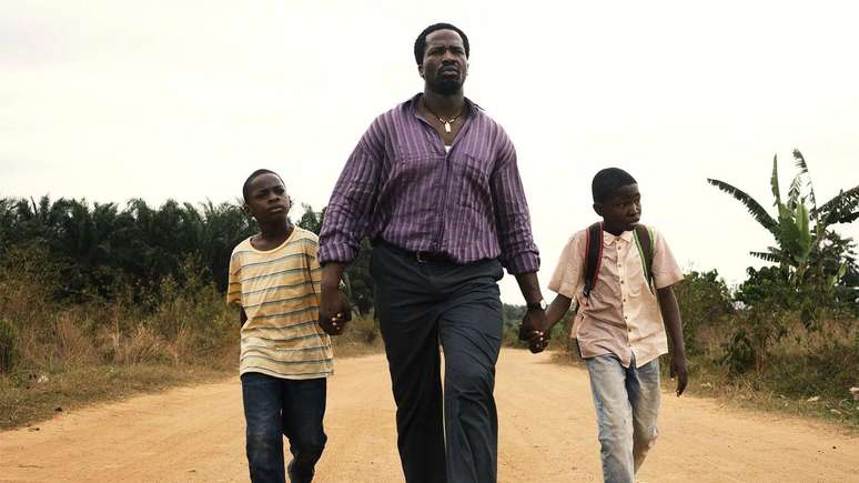 Homem caminhando em rua de terra de m&atilde;os dadas com os dois filhos 