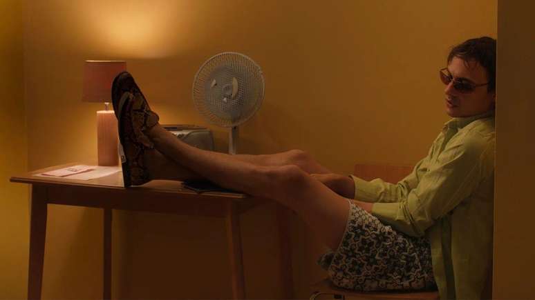 Homem sentado em cadeira com os p&eacute;s apoiados em cima de uma mesa